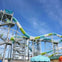 A tall water slide with green and blue sections supported by a metal structure under a clear blue sky.