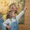 A woman and a young child point and look up while indoors, with a blurred painting in the background.