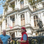 Two men stand in front of a historic building with a statue and an American flag, engaging in conversation on a sunny day.