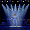 A performer in a blue suit and hat sings passionately on a stage under spotlights, with a band and "Sinatra" script behind.