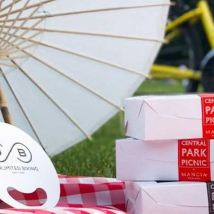A picnic setup with a white parasol, stacked boxes labeled "Central Park Picnic," and part of a bicycle visible.