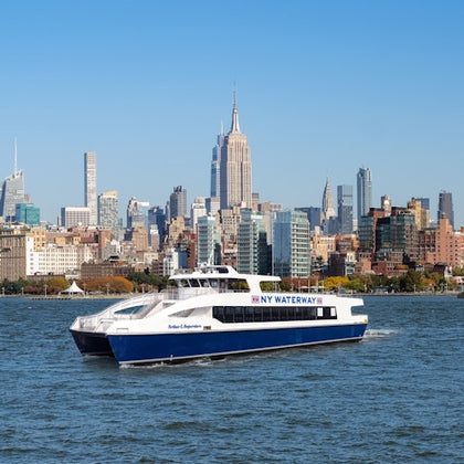 A ferry labeled 'NY Waterway' traveling on a river, with the Manhattan skyline, including the Empire State Building, in the background.