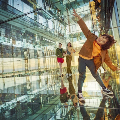 Three people in a reflective, glass-filled room, with one leaning playfully toward the camera.