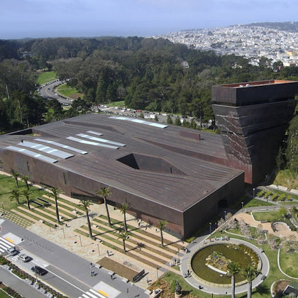 Large, modern building with a unique angular design, surrounded by greenery and roads, with a distant cityscape in the background.