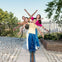 Four people stand in a line with their arms outstretched, smiling, and posing by a fenced area in a park with cobblestone paths and trees.