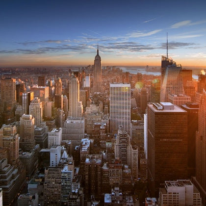 Aerial view of a city skyline with numerous skyscrapers, including a prominent, pointed building, during sunset.