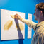 A person interacts with a tactile exhibit on a blue wall, touching a display featuring raised yellow shapes.