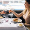 Two people seated at a restaurant table by a window, toasting drinks over a meal, smile and engage in conversation.