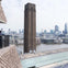 A tall brown tower with a cityscape view in the background, seen from a building's balcony overlooking a river.