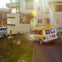 A van with a yellow canopy parked on a brick driveway near a beige building, with sunlight creating lens flare effects.