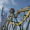 A roller coaster with a yellow track and steel supports, featuring a steep drop and a loop, under a clear blue sky.