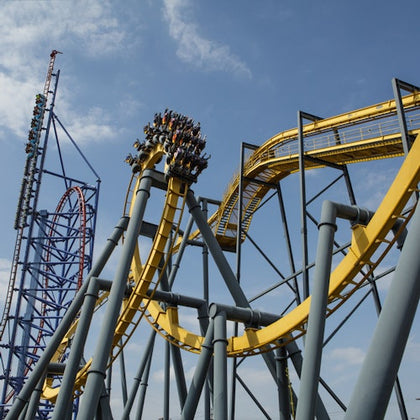 A roller coaster with a yellow track and steel supports, featuring a steep drop and a loop, under a clear blue sky.