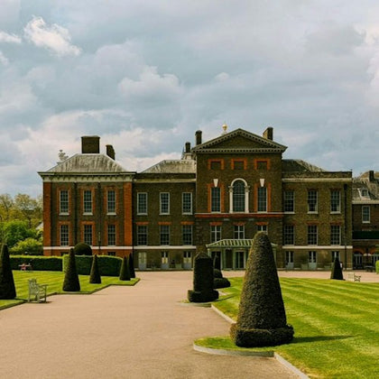 A historic building with brick and stone architecture surrounded by a landscaped garden with trimmed hedges and pathways.
