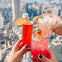 Three hands holding colorful cocktails with a city skyline in the background.