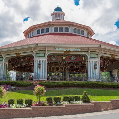 A large carousel housed in an ornate pavilion with a red roof, surrounded by landscaped greenery and flowers.