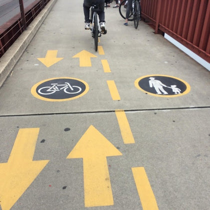 A shared pedestrian and bike path with painted symbols and arrows, showing lanes for bicycles and walkers.