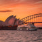 A cruise ship in front of the Sydney Opera House and Harbor Bridge during a vibrant orange sunset.