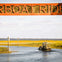 An airboat navigates a waterway surrounded by marshland, beneath a wooden "Airboat Ride" sign.