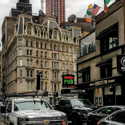 Urban street scene with a historic building, cars parked, and signs for O'Reilly's Pub. Flags are seen on the right.