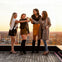 Four women standing on a rooftop terrace at sunset, clinking glasses in a celebratory toast.