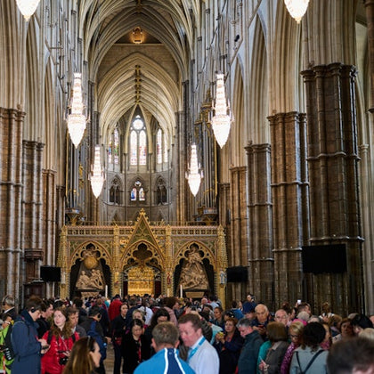 Interior of a large cathedral with arched ceilings, chandeliers, ornate decorations, and a crowd of people walking through.