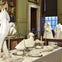 An ornate room with a table set with intricately folded white napkins and gowns displayed on mannequins in the background.
