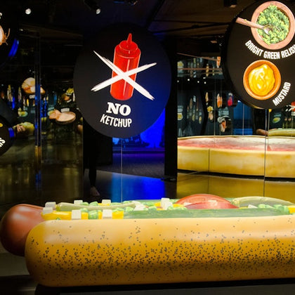 A giant model of a Chicago-style hot dog with a "No Ketchup" sign in a museum exhibit featuring various condiment displays.