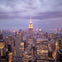 A cityscape view of Manhattan at dusk, featuring the Empire State Building illuminated against a cloudy sky.