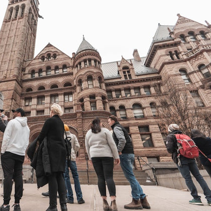 People standing and talking in front of a large, historic building with detailed architecture and a clock tower.