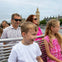 A group of people, including children and adults, sitting on a boat with Big Ben and the Houses of Parliament in the background.