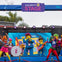 Performers in colorful costumes resembling LEGO characters dance and sing on a stage under a banner reading "The Brick Stage."