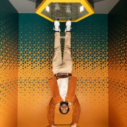 A person is positioned upside down in a room with patterned gradient walls, creating a visual illusion.