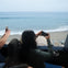 People in a vehicle by the ocean, taking photos of the beach and waves through the open window.