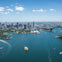 Aerial view of a city skyline by a harbor, featuring a prominent bridge and an iconic white architectural structure.