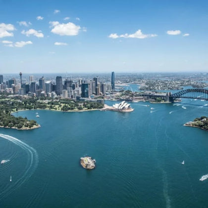 Aerial view of a city skyline by a harbor, featuring a prominent bridge and an iconic white architectural structure.