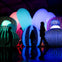 Silhouetted people walk among large glowing inflatable sculptures with colorful patterns in a dark exhibit space.