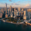 Aerial view of a helicopter flying over the waterfront near skyscrapers in downtown Manhattan at sunset.
