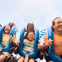 Three people seated on a roller coaster ride, holding handles, and expressing excitement and thrill.