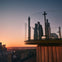 Two people stand on a circular glass observation deck at sunset, overlooking a city skyline with a clear sky.