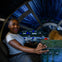 A person smiles while sitting in a spaceship cockpit, with a blue, star streaked view through the windshield.
