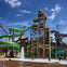 A water park with slides, a skull-themed structure, and people enjoying the pool under a sunny sky.