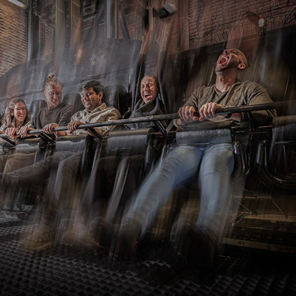 People on an amusement ride, gripping safety bars, with expressions of excitement and fear. Motion blur suggests fast movement.
