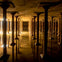 A dimly lit underground structure with rows of columns reflected in standing water on the floor.