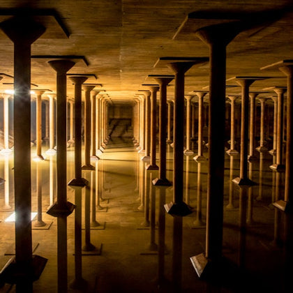 A dimly lit underground structure with rows of columns reflected in standing water on the floor.