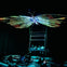 People are seated and lying on the floor under a large, glowing butterfly sculpture in a dark room.