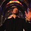 A man in a black suit conducts with closed eyes in a colorful, illuminated cathedral.