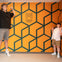 Two people posing in front of an orange wall with a geometric pattern and the text 'Museum of Illusions Denver.'