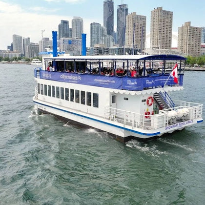 A sightseeing boat named 'Showboat Royal Grace' on a body of water, with a city skyline and tall buildings in the background.