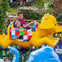A man and a child ride a bright yellow elephant-themed ride with colorful patchwork details, smiling and enjoying the moment.