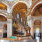A grand interior of a cathedral with ornate decorations, high arches, detailed ceilings, and a lit altar with candles.